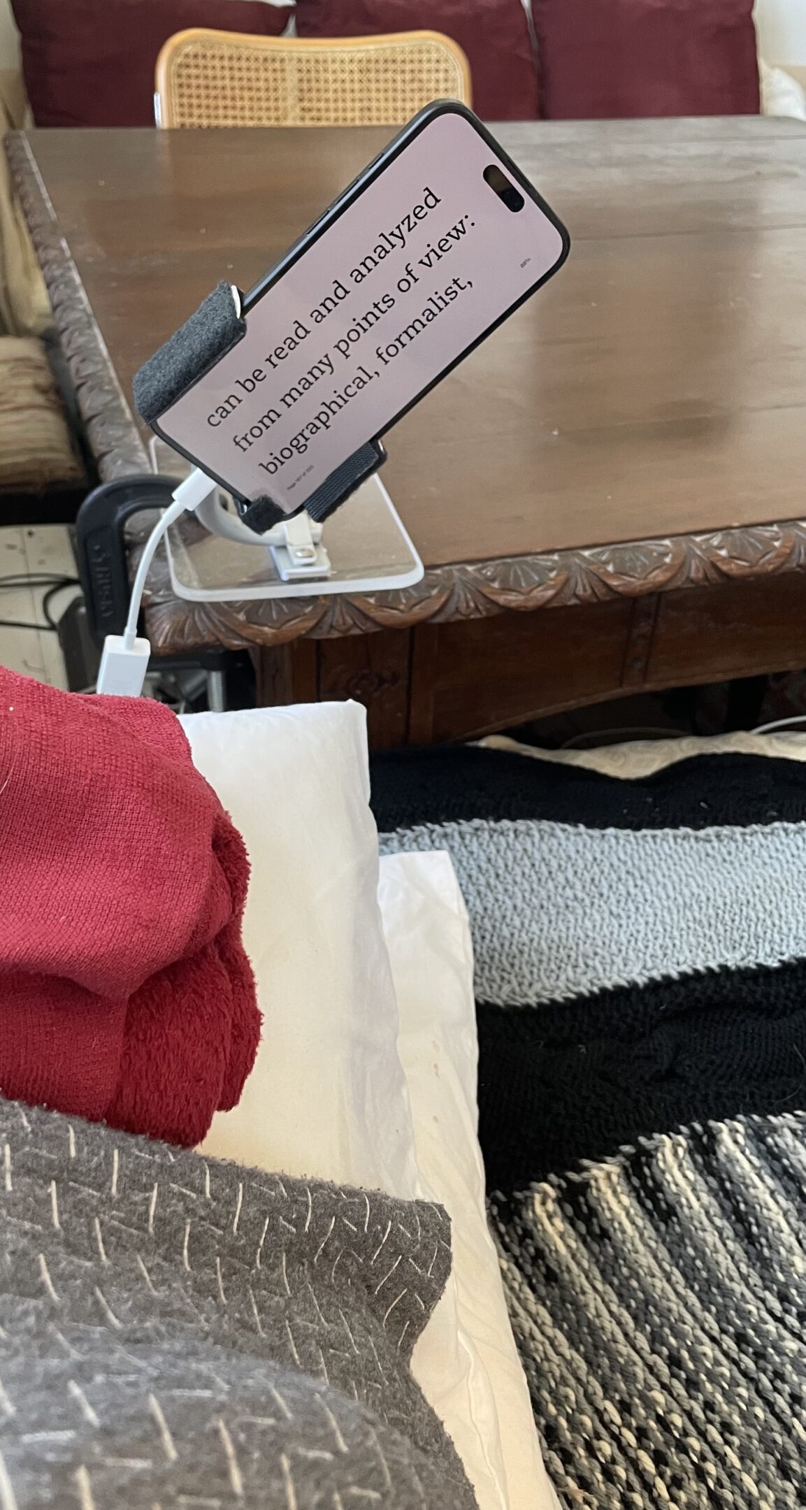 A red hoodie, white pillow, and a phone charging on a table.