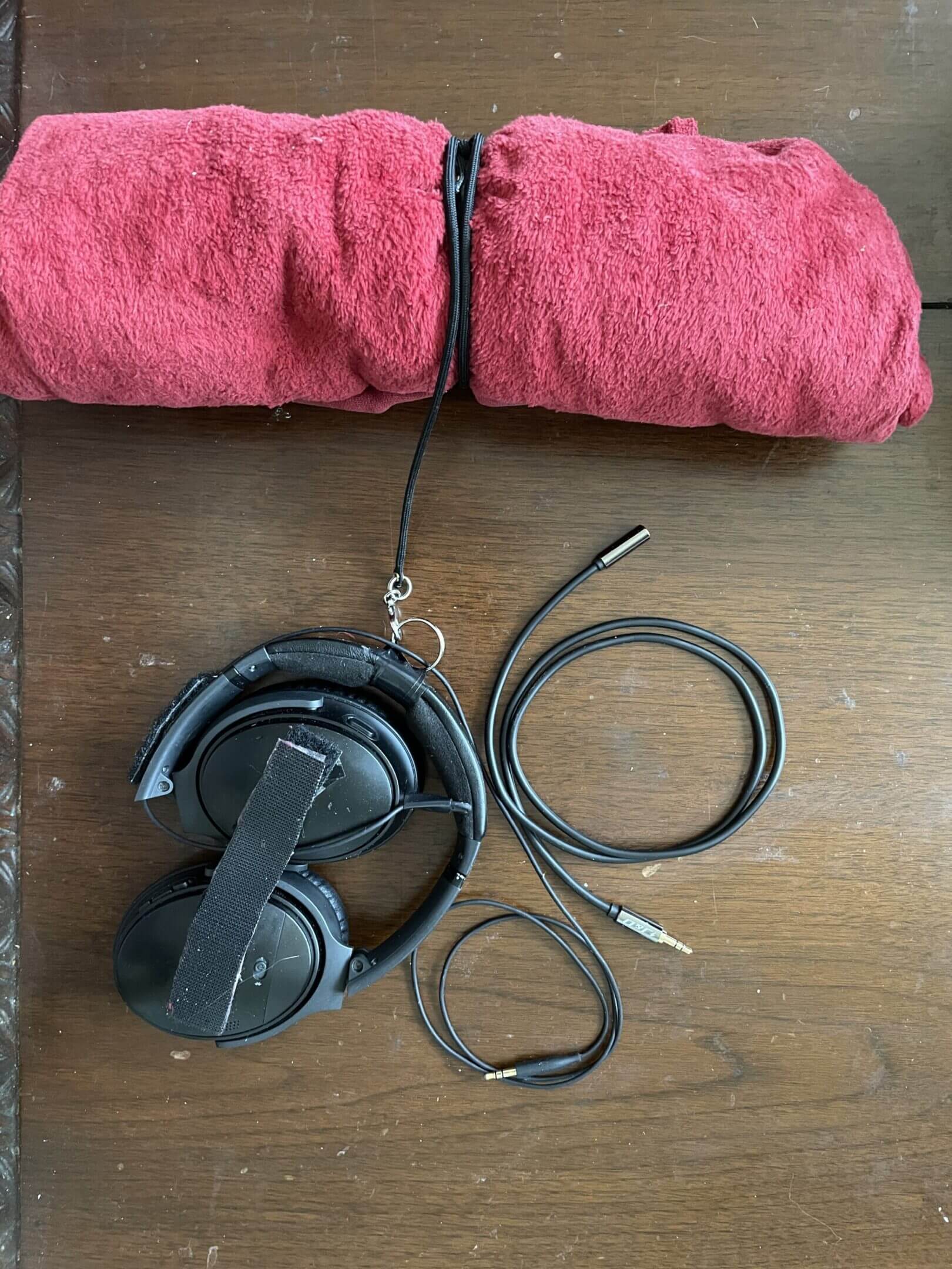 Black wired headphones placed on a wooden surface with a red fabric item nearby.