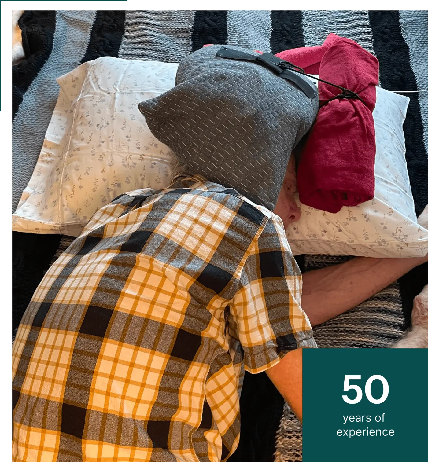 Person lying face down with a gray pillow on their head, wearing a plaid shirt. Text on the image reads "50 years of experience.
